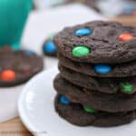 Close up image of a stack of chocolate m and m cookies on a white plate.