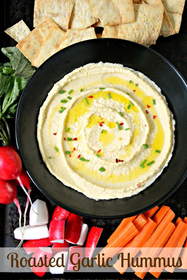 Hummus in a bowl surrounded by fresh vegetables.
