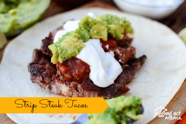 Slices of seared strip steak is piled on top of a tortilla wrap, with sour cream and guacamole topping it off for this Steak Taco Recipe.