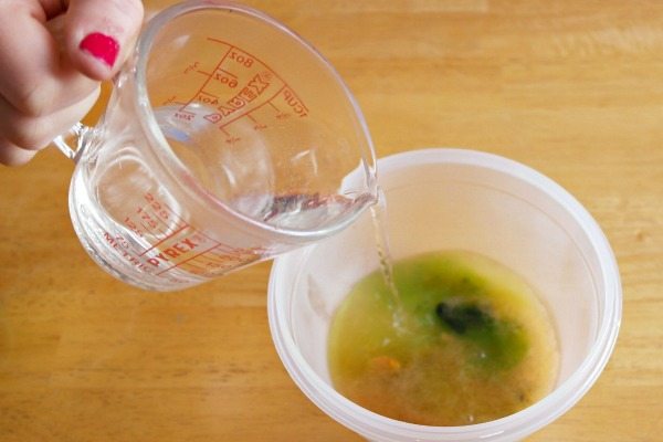 a woman's hand pours water from a measuring cup into a small bowl