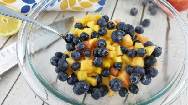 Fresh blueberries and peaches in a bowl with a spoon.