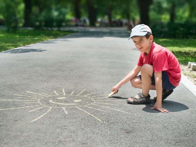 Child using chalk to draw sun on asphalt in a park