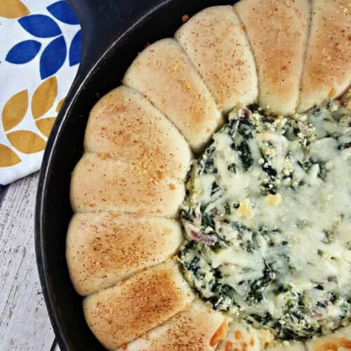 Cheesy Spinach Dip with garlic bread rolls in a cast iron skillet.