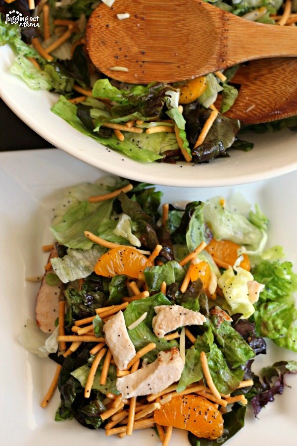 A large white bowl filled with Mandarin Orange Salad at the top of the image, with a white plate piled with the salad including Chow Mein noodles, slivered almonds, and chicken on romaine and red leaf lettuce topped with a poppyseed dressing.