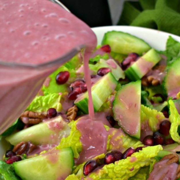 close up of pitcher pouring pomegranate dressing onto a bowl of salad