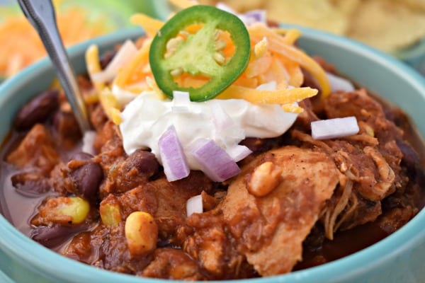 Close up image of Best Ever Slow Cooker Chicken Chili in a bowl, topped with sour cream, cheese, jalapeno, and onions. 