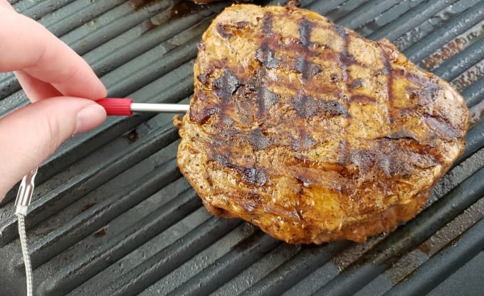 A hand places the Weber iGrill mini probe into a petite sirlon steak on a grill pan.