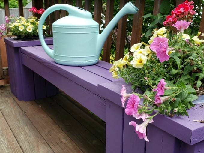 Watering can on top of an outdoor planter bench.