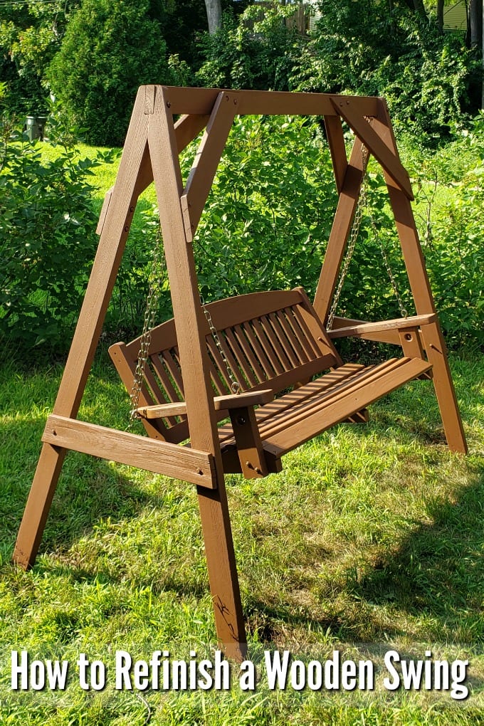 An newly painted A frame swing on a lawn in front of a row of bushes.