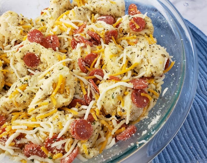 Mixture of dough, cheese, mini pepperoni, and seasonings tossed together in a clear bowl.