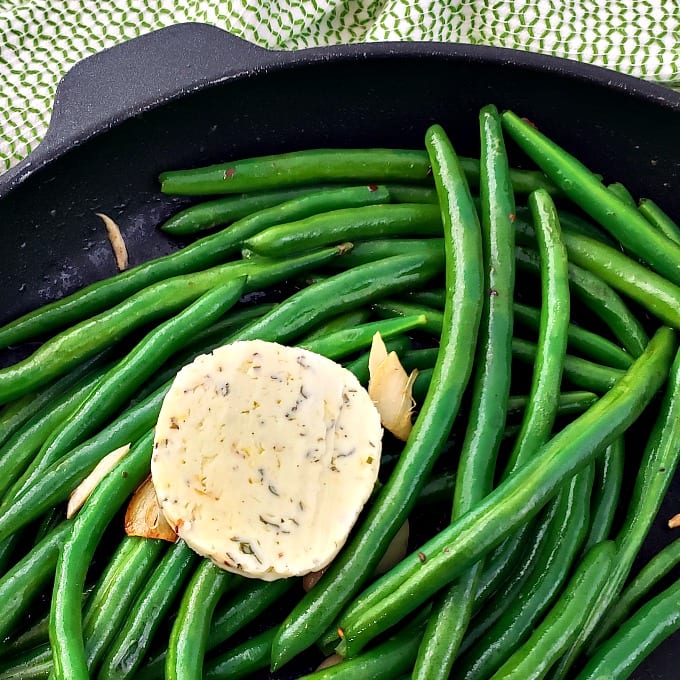 Cast iron skillet filled with green beans topped with cowboy butter.