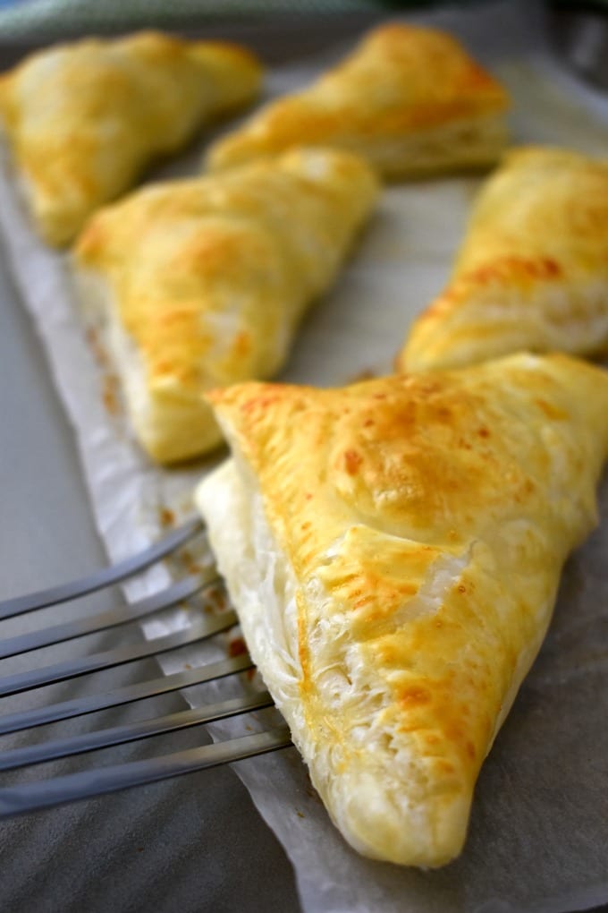 Golden brown Puff Pastry stuffed with creamy swiss cheese, garlic and herbs on a sheet tray lined with parchment paper. 