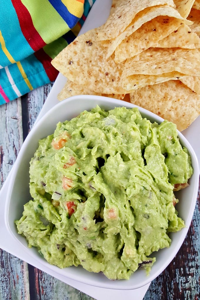 A bowl of guacamole with tomatoes and red onions next to tortilla chips.