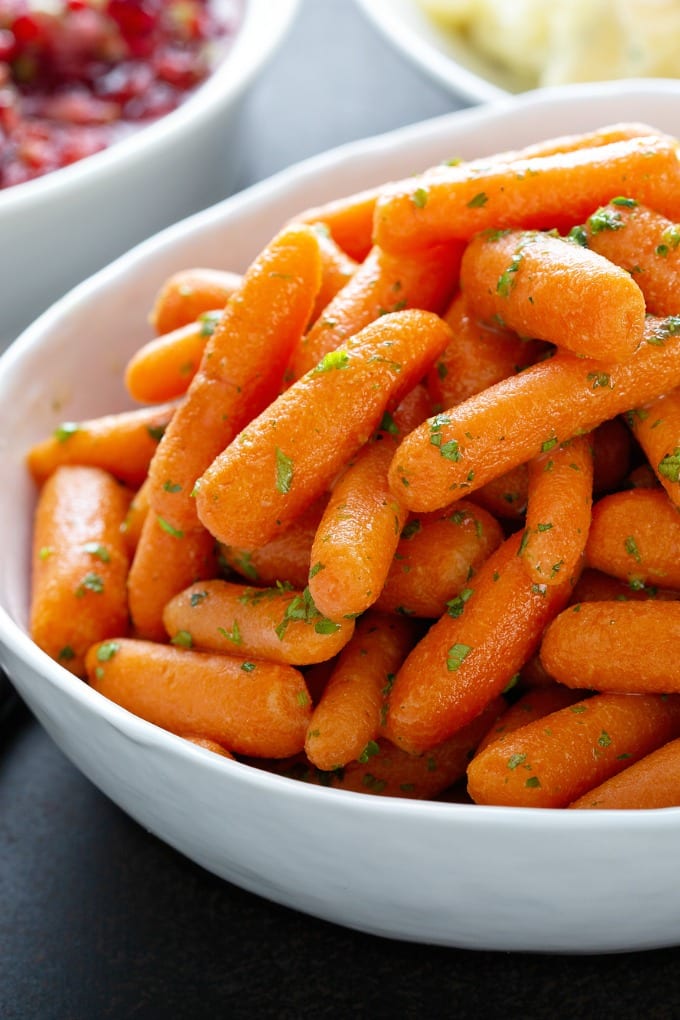 A white bowl of honey glazed baby carrots with tarragon.