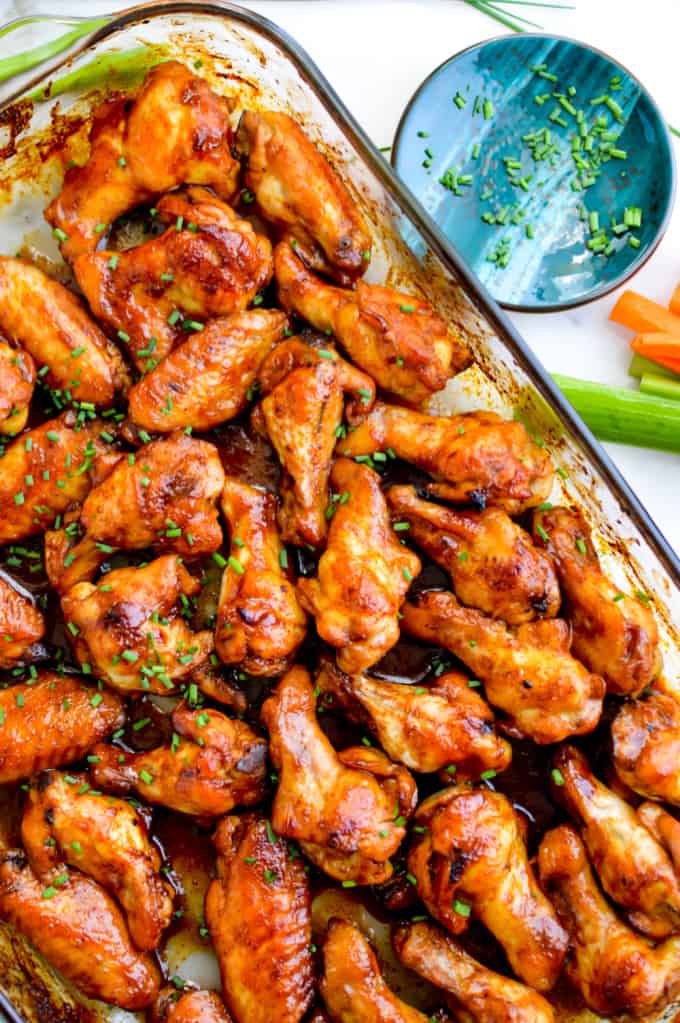 Baked honey teriyaki wings in a clear baking dish, garnished with chives.