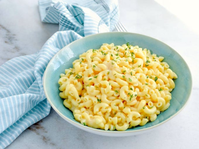 Mac and Cheese in a blue bowl on a table with a blue and white kitchen towel