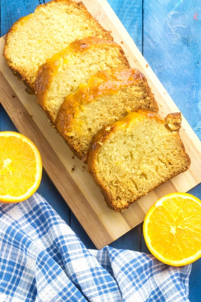 Orange Pound Cake Recipe - slices of orange pound cake on a cutting board near halved oranges and a blue and white kitchen towel