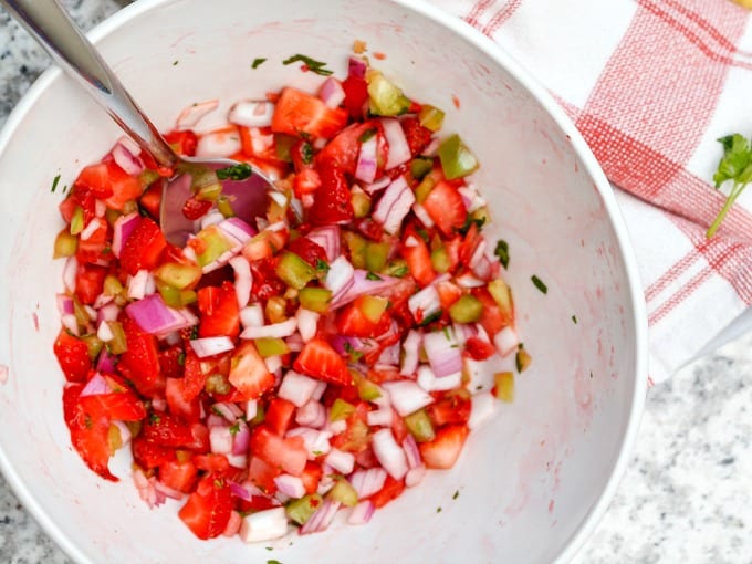 Strawberries, red onion, jalapeño, cilantro, lime and sea salt in a large mixing bowl with a metal spoon.