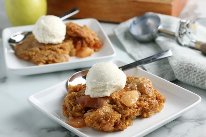 Two square plates of slow cooker apple cobbler topped with ice cream.
