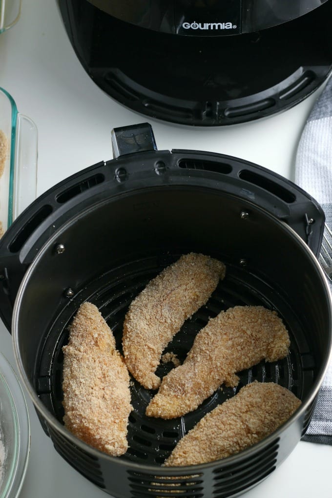 Chicken tenders in the basket of an air fryer before cooking.