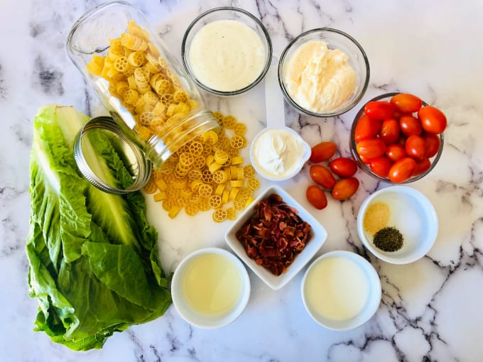 Ingredients to make a BLT pasta salad - romaine, pasta, red onion, bacon, ranch dressing, mayonnaise, cherry tomatoes, salt and pepper, bacon, sour cream, milk and garlic powder.
