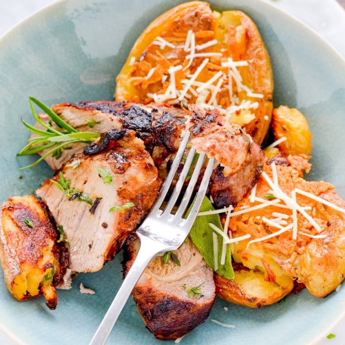 Image of grilled pork tenderloin served with crispy smashed potatoes on a blue plate with a fork.