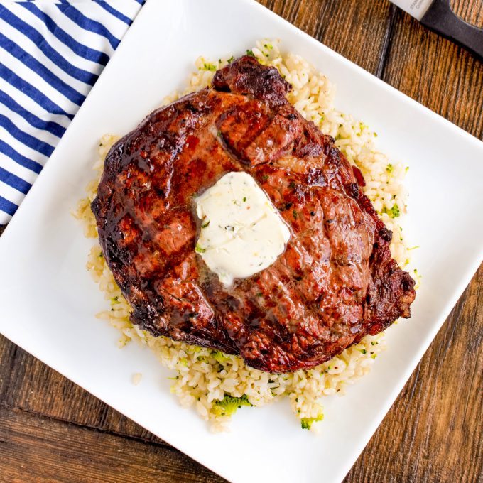 Best grilled ribeye topped with cowboy butter sitting on a bed of broccoli rice on a white plate.