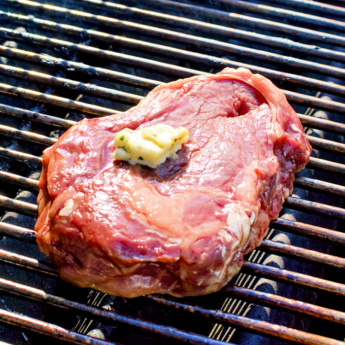 Steak on the grill topped with seasoned butter.