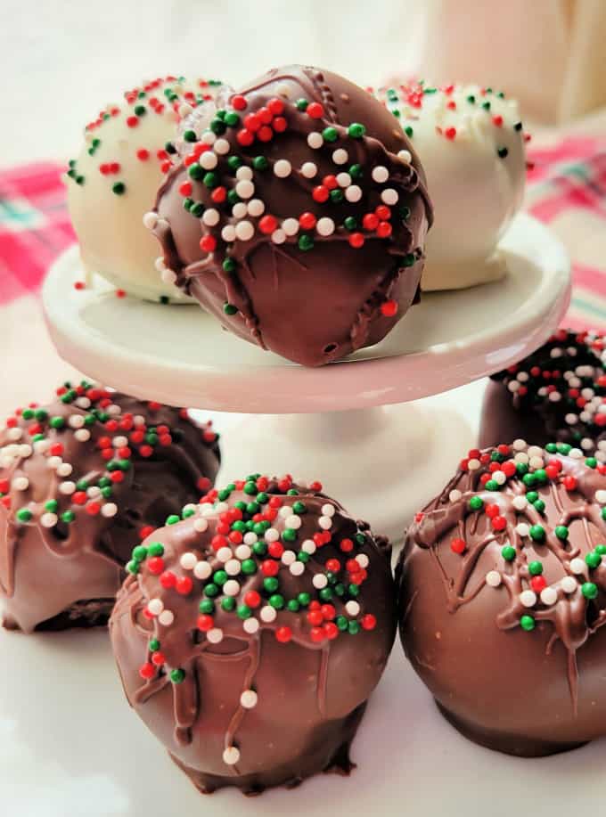 Brownie truffles covered in chocolate and red and green sprinkles on a white cake stand.