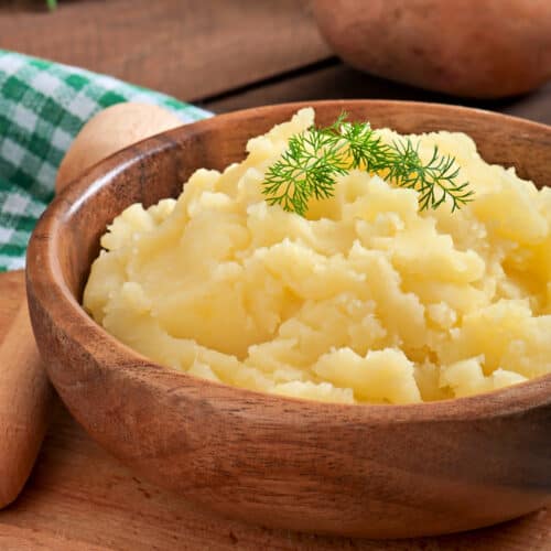 Square, close up image of mashed potatoes in a wood bowl.