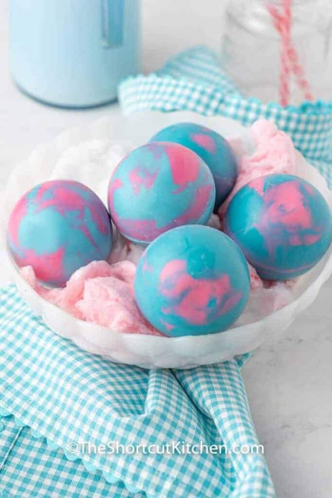 A white bowl, filled with pink cotton candy and blue and pink hot cocoa bombs.