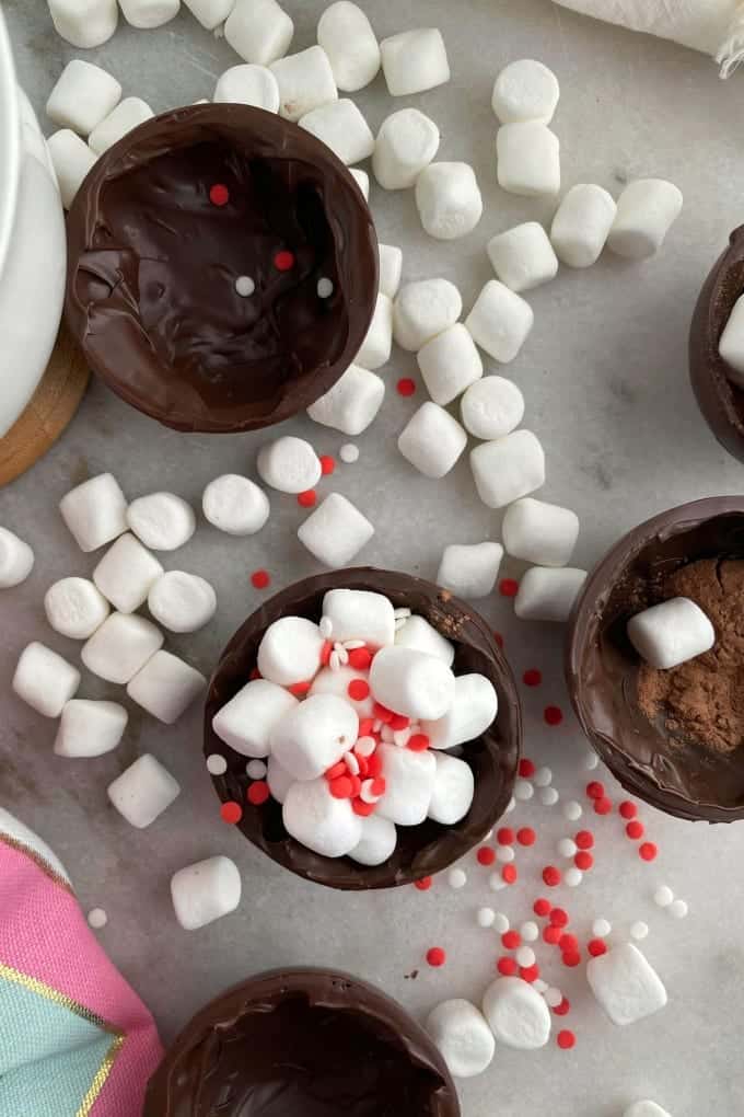 Close up, top down image of a hot chocolate ball split in half and filled with mini marshmallows and sprinkles. 