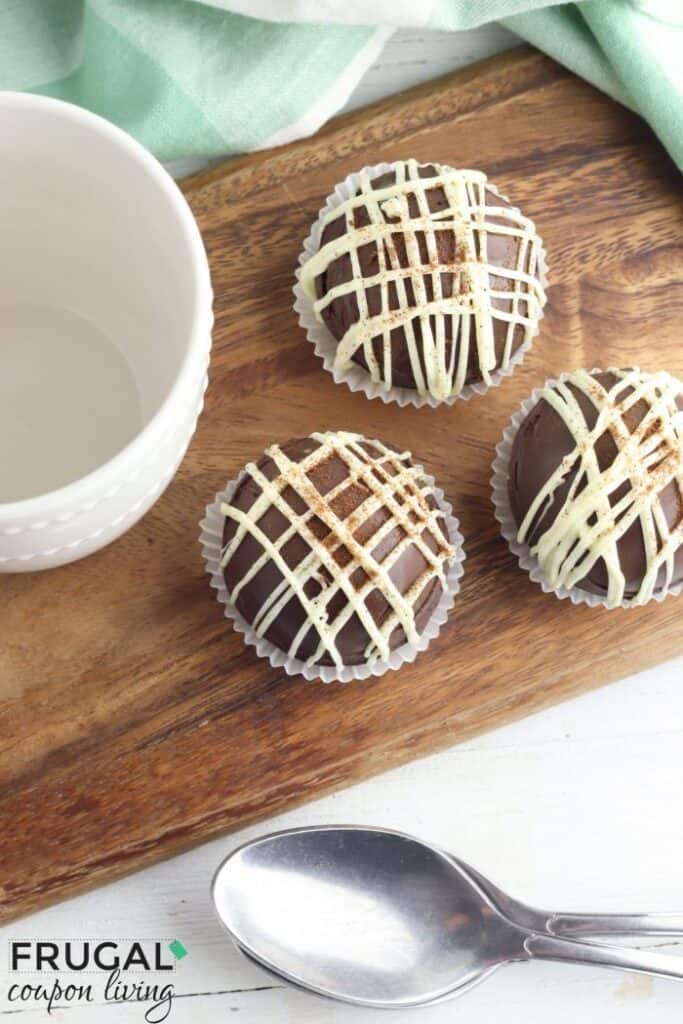 Top down view of white chocolate drizzled mocha coffee bombs in small white muffin cups on a wooden cutting board.