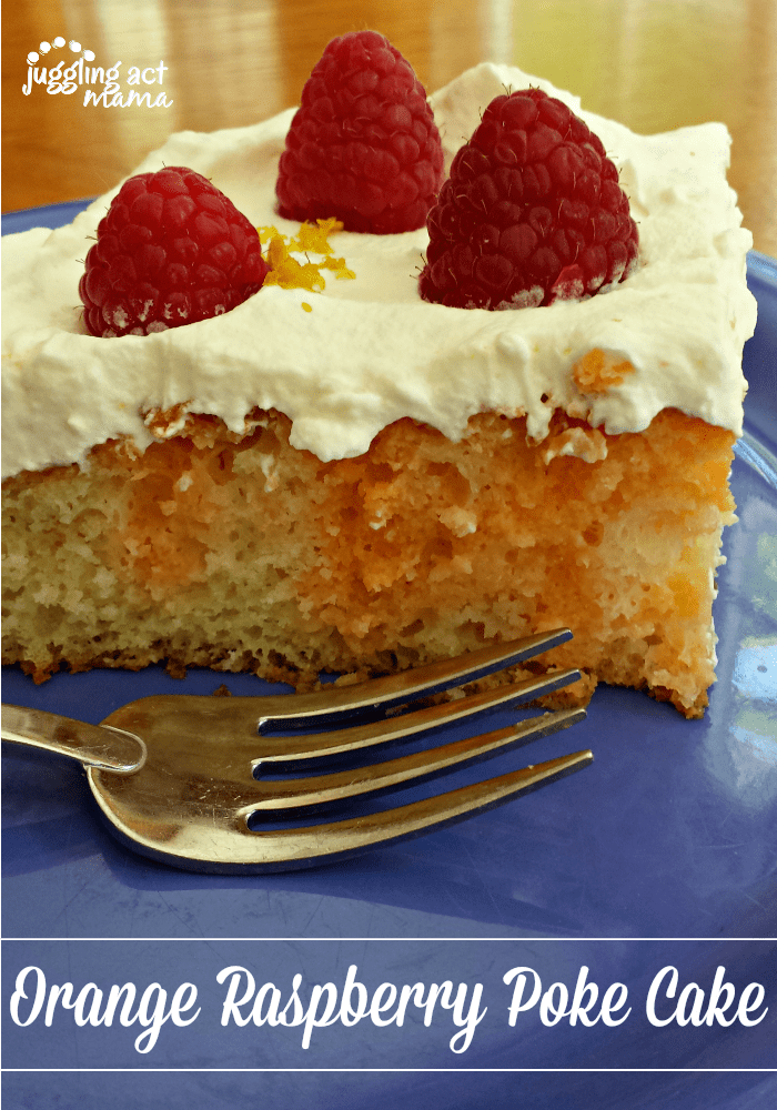 Close up image of a slice of raspberry poke cake topped with fresh berries, orange zest and homemade whipped cream.

