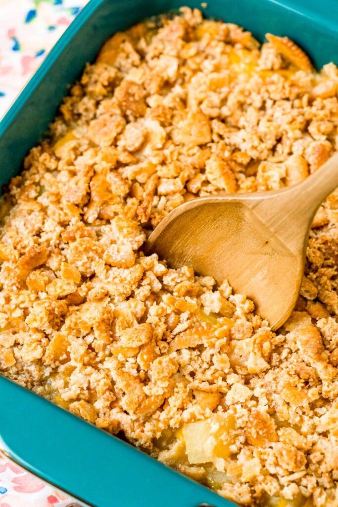 Pineapple casserole being scooped from a casserole dish by a wooden spoon.