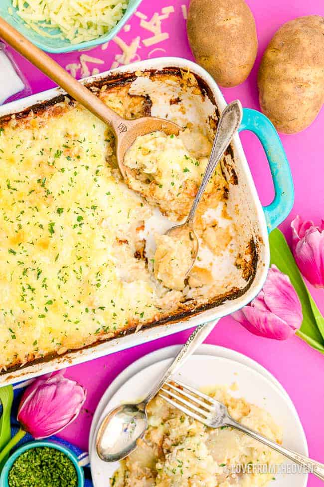 Top down image of a casserole dish filled with scalloped potatoes next to a plate and silverware.