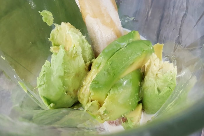 a top down view of a whole banana, and avocado with milk yogurt and honey in a blender