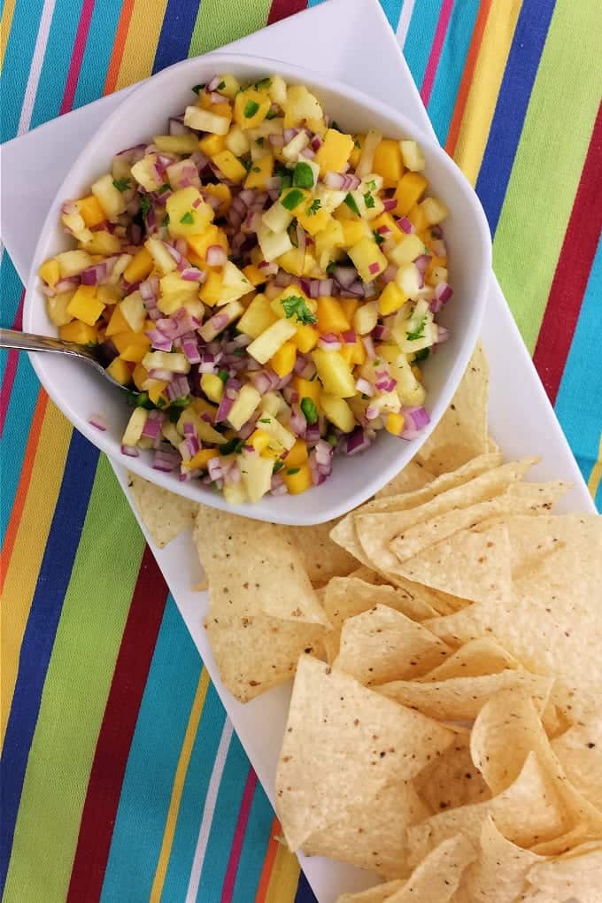 Top down view of pineapple mango salsa in a white bowl with a spoon next to tortilla chips.