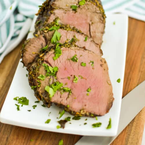 Sliced Petite Sirloin Roast, garnished with parsley, on a white serving platter.