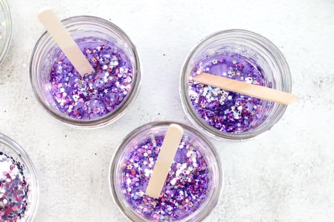 stirring jars with craft stick to spread out the glitter