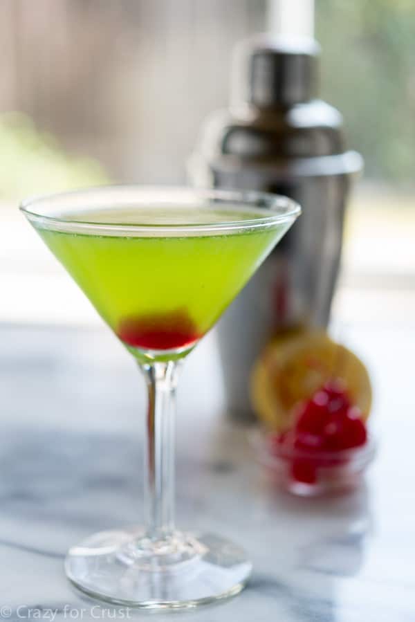 Midori martini garnished with a simple cherry, shaker in background