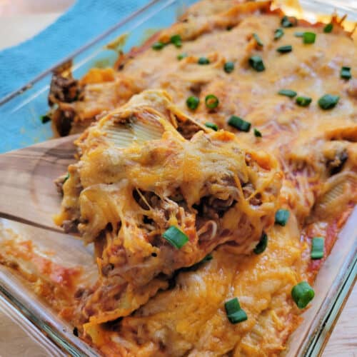 Square cropped image Taco Stuffed Shells in a casserole dish with a wooden spoon.
