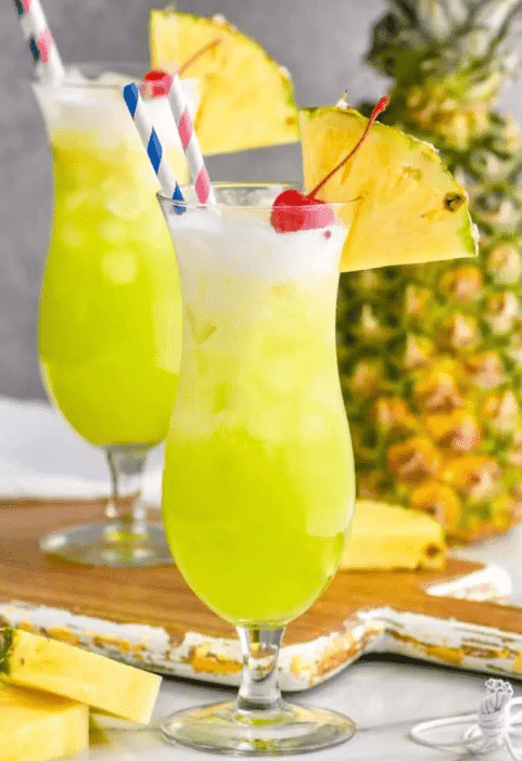 two glasses of Midori splice garnished with pineapple wedges and cherries