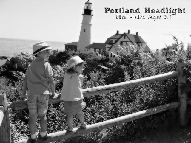 Black and white image of the Portland Head Light behind two children standing on a fence.