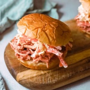 Two pulled pork sandwiches on a wooden cutting board.