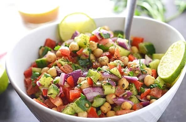 Chickpea Salad in a bowl with a spoon and a wheel of lime.