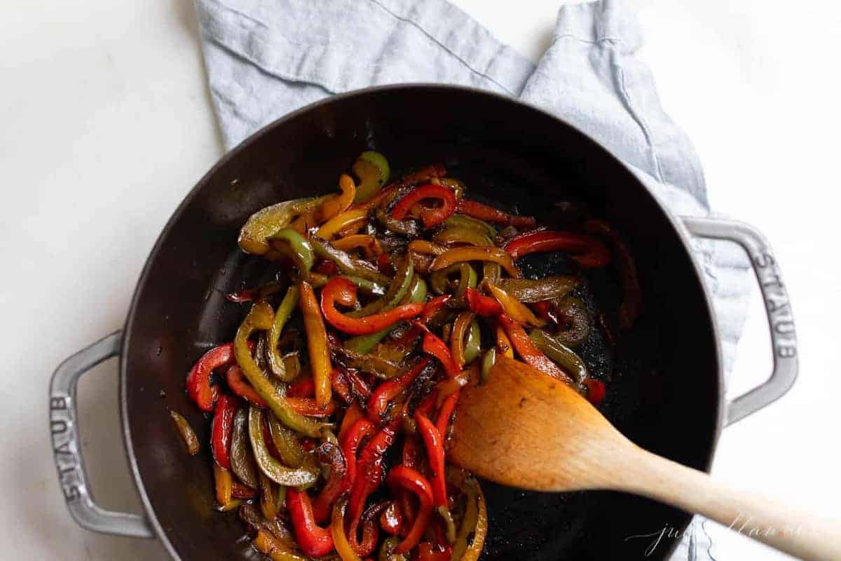 Sautéed Bell Peppers in a pan with wooden spoon stirring.