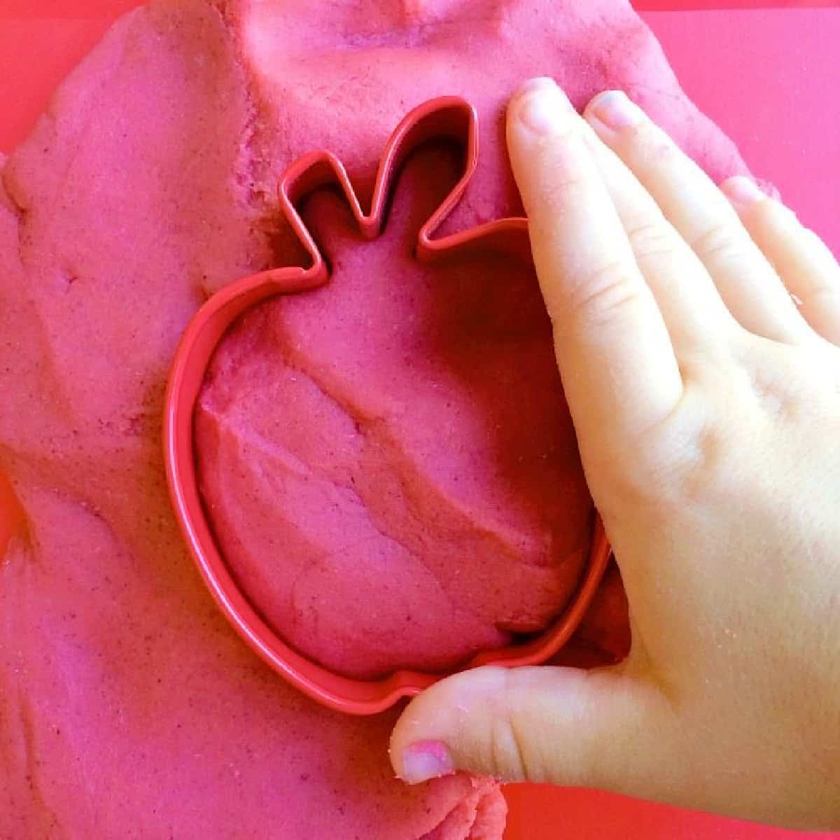Child's hand on an apple cookie cutter pushed into play dough.