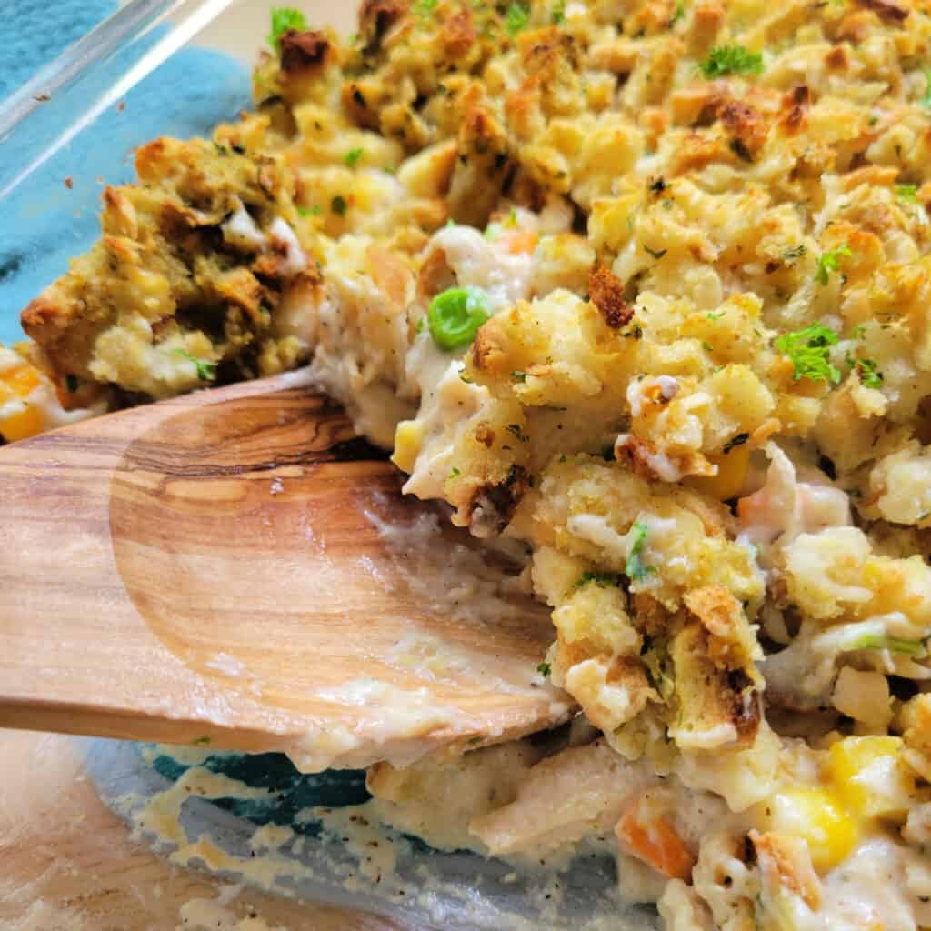 Close up of creamy Chicken Stuffing Bake in a casserole dish with a wooden spoon.