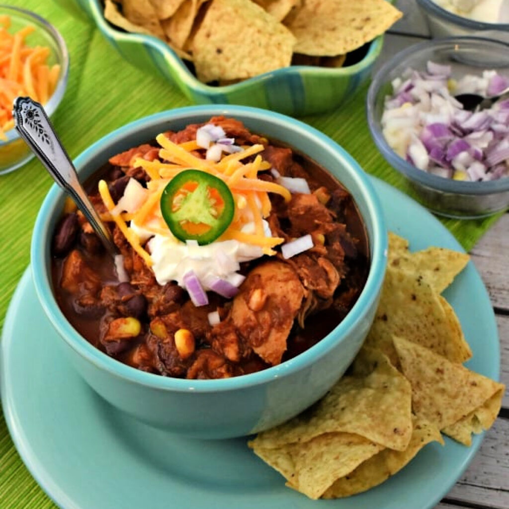 Close up of Slow Cooker Chicken Chili in a bowl with sour cream, cheese, and chips.